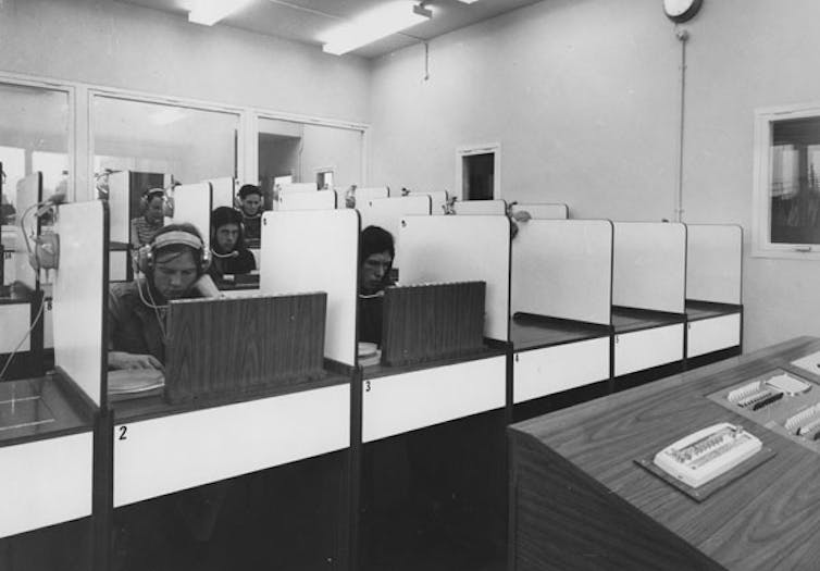 People wearing headphones sit in booths, each looking at a screen.