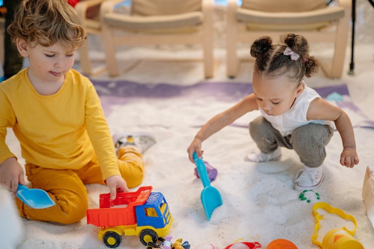 Two children seen playing with sand.