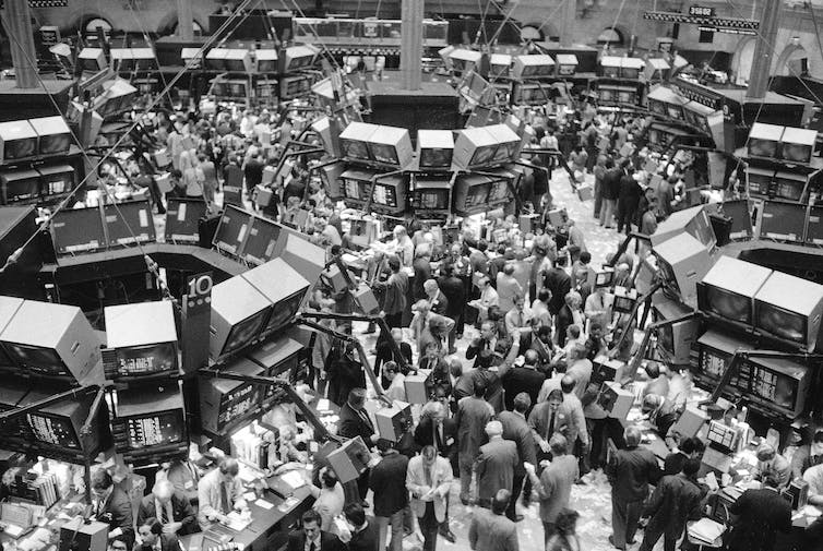 a crowd of people move around a large room with big screens all over the place