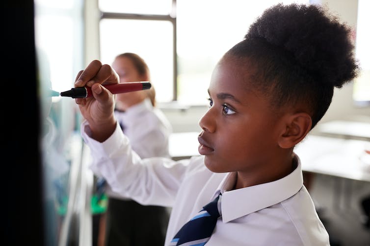 A young girl works at a whiteboard.