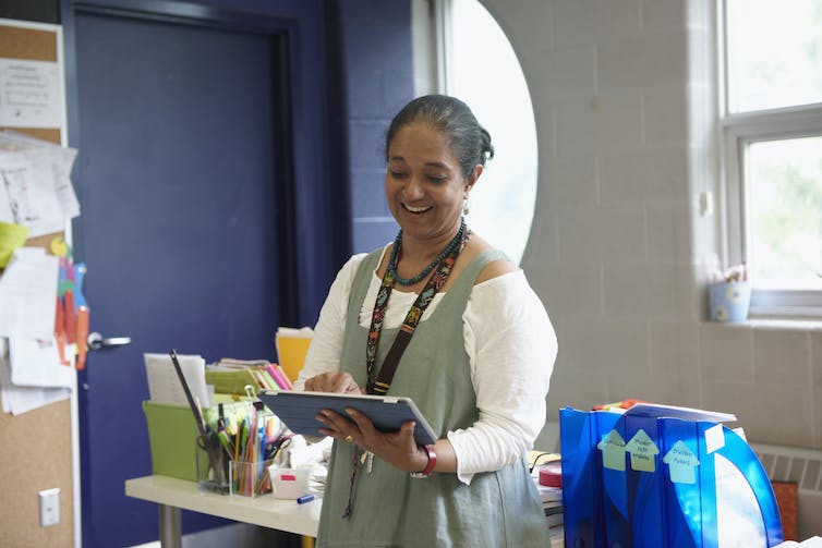 Teacher holds tablet while working in classroom