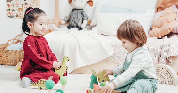 Two children seen sitting on a carpet playing