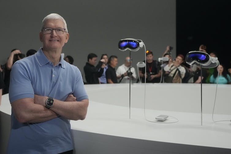 A white man in a polo shirt poses in front of a displayed VR headset