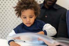 A child seen with an adult reading a book.