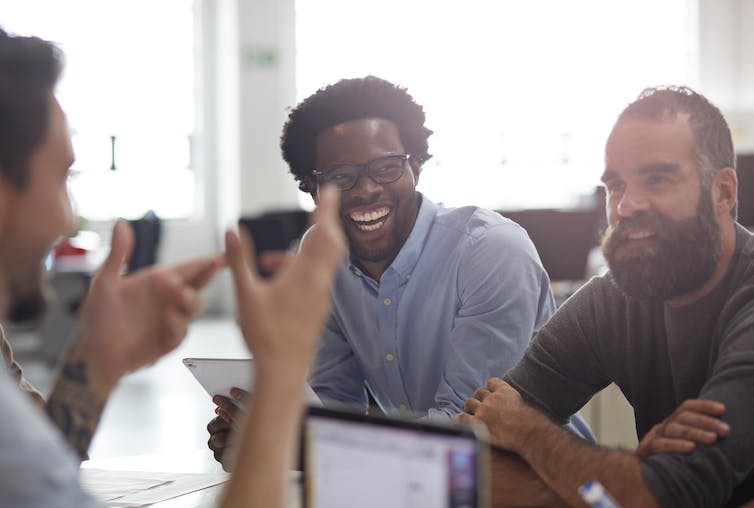 three men talking and laughing in an office setting