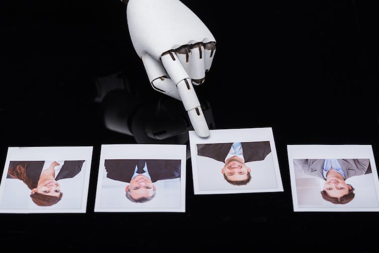 a robot hand points to one of four photographs on a shiny black surface