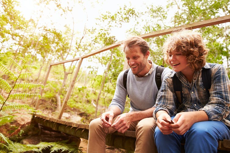 Adult man and teenagers sitting on bridge outdoors