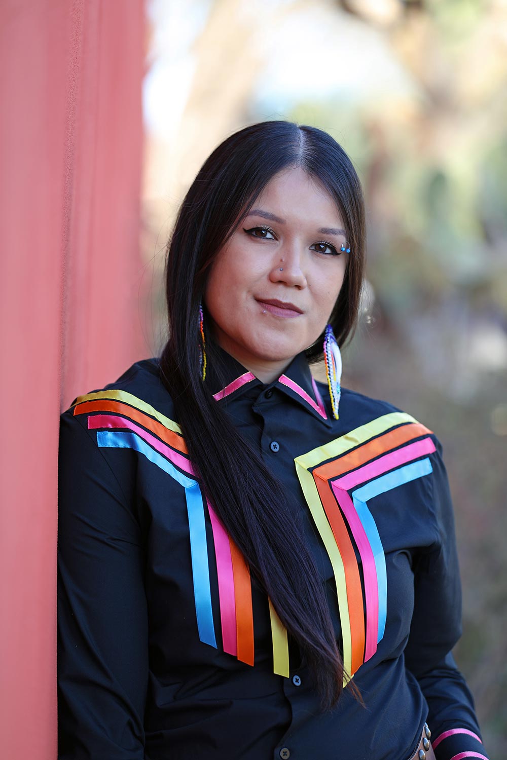 Portrait of artist Kaylene Big Knife wearing a black dress shirt with colorful ribbons.