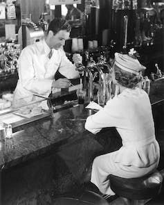 Soda fountain attendant serving young woman in a black and white photo taken in the 1950s