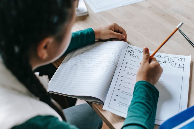 A child writes in a workbook at a desk.