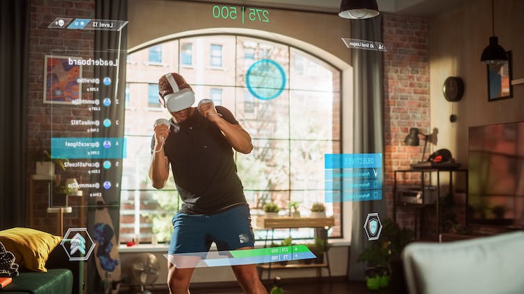 Man standing up and using a virtual reality headset and handheld controls in a living room.