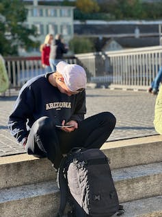 A teen with skateboard looking at phone.