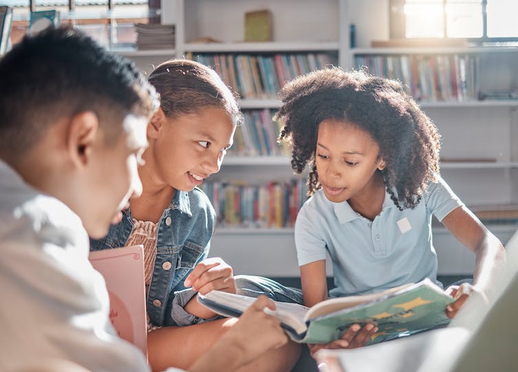 A group of children read a book together.