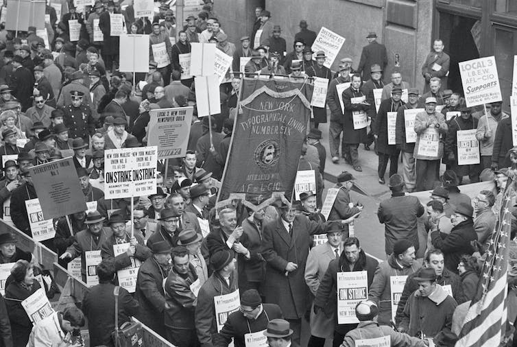 Dozens of protesters with the ITU stand densely packed together on a New York City street, waving signs and placards.