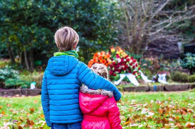 Brother comforting younger sister near grave