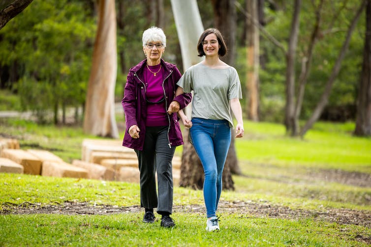 Annelise and Alix walking outside on grass, trees in background