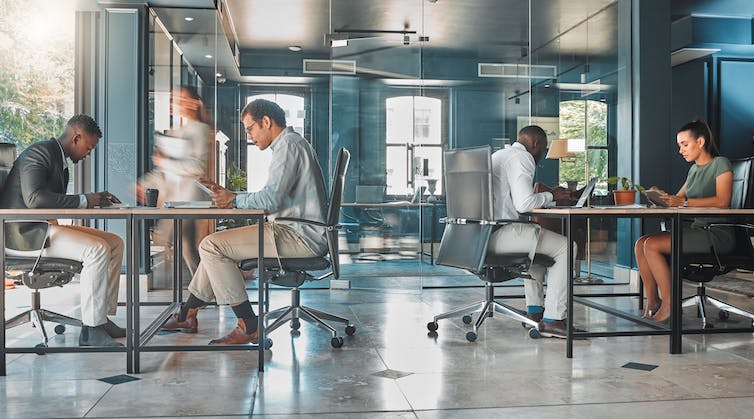 four people sitting around two tables in a coworking space