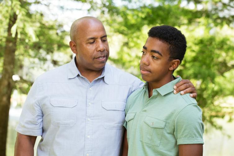 A man with his arm around a teen, outdoors