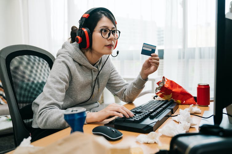 A woman wearing headphones and holding a credit card looks at a computer screen