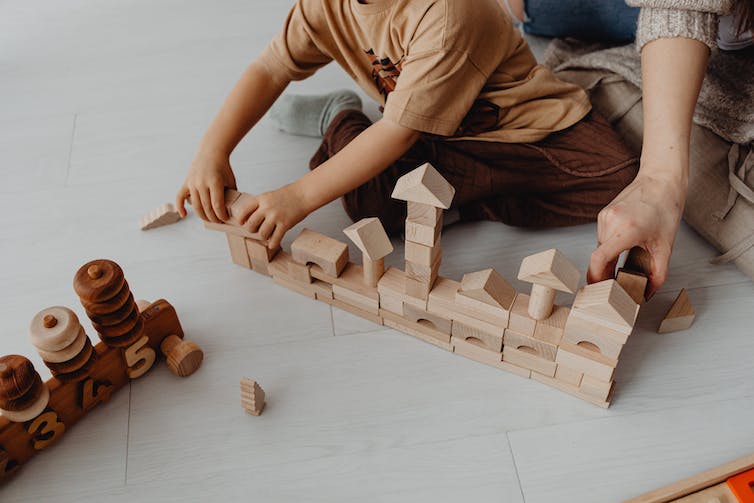 An adult and child play with wooden blocks.