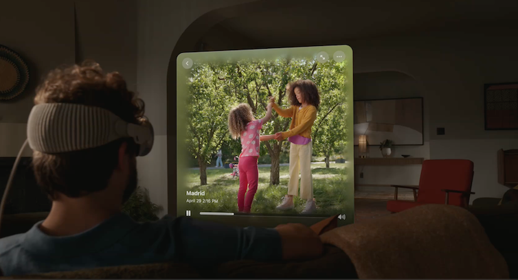 A man sitting on a couch wearing a headset while an image of children playing floats in the air in front of him.