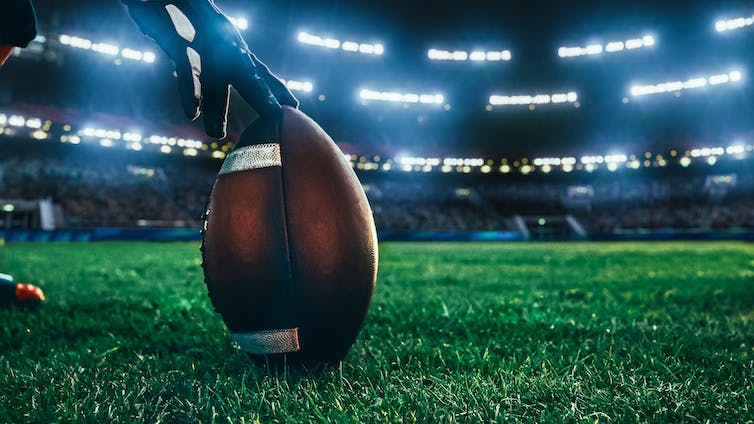 A gloved hand holds a football on a grassy surface