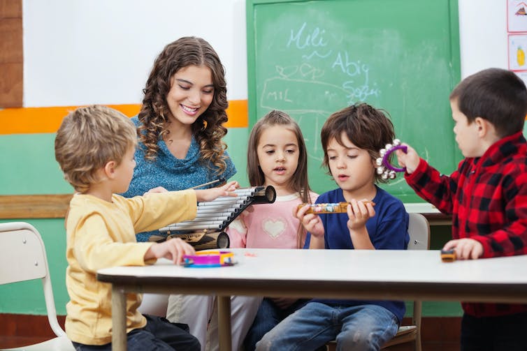 An educator seen at a table with children with musical instruments.