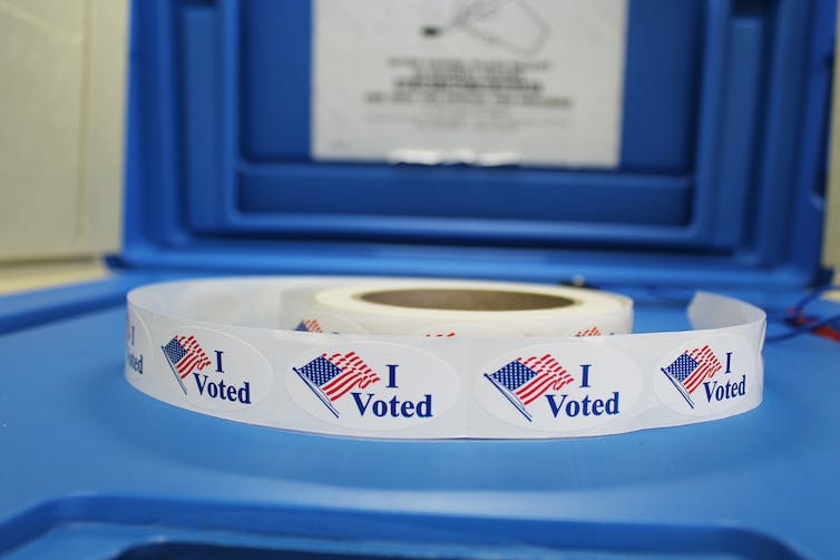 A roll of stickers reading 'I voted' next to a a picture US flag.