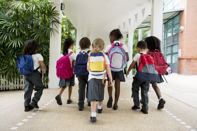 Young school children in uniform walking away from camera