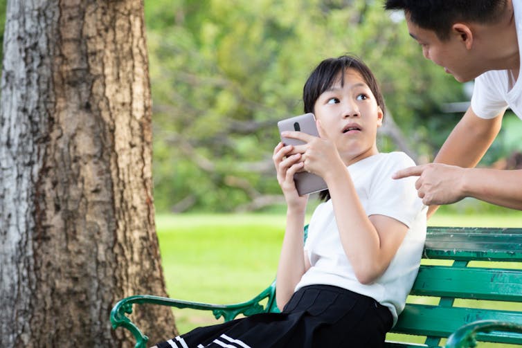 A girl looks surprised while her dad talks to her about phone use.