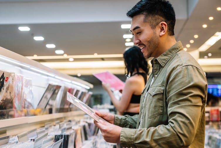 A young man smiles while browsing a selection of vinyl records in a shop