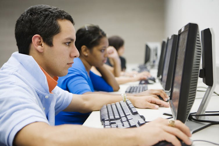 A row of students in a uni computer lab looking at screens.