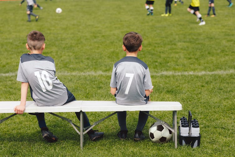 Two boys sat on sidelines of football match