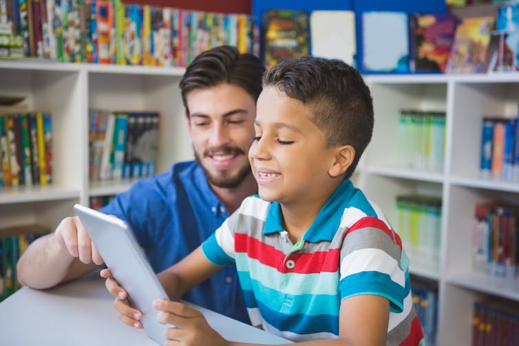 Man and boy reading from tablet in library