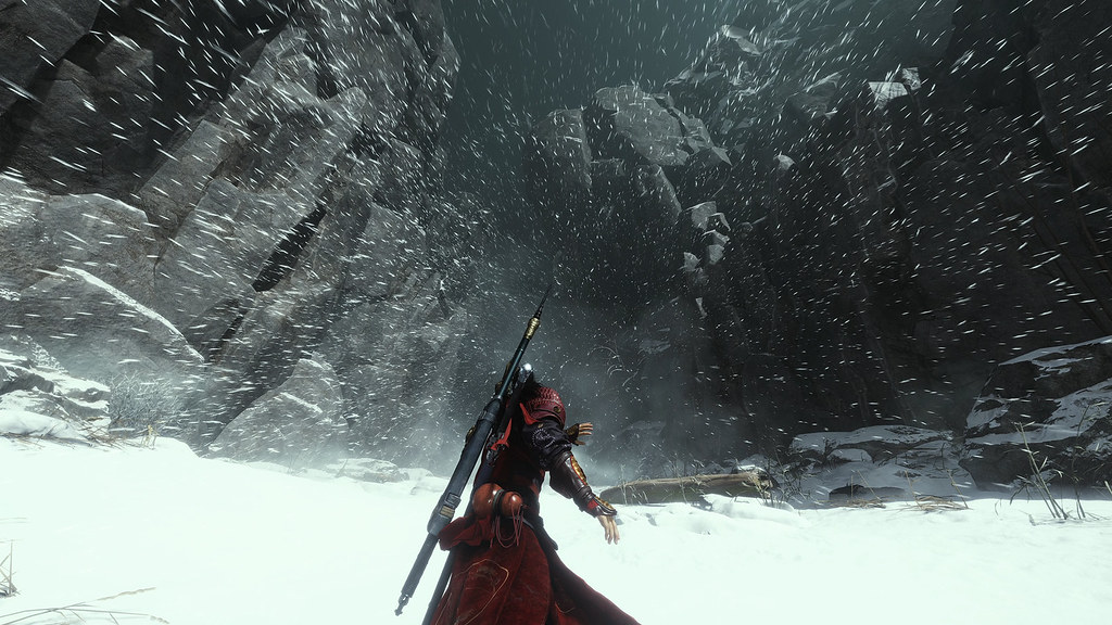 In this image, a red-clad figure battles against a high wind as they walk through an icy canyon.