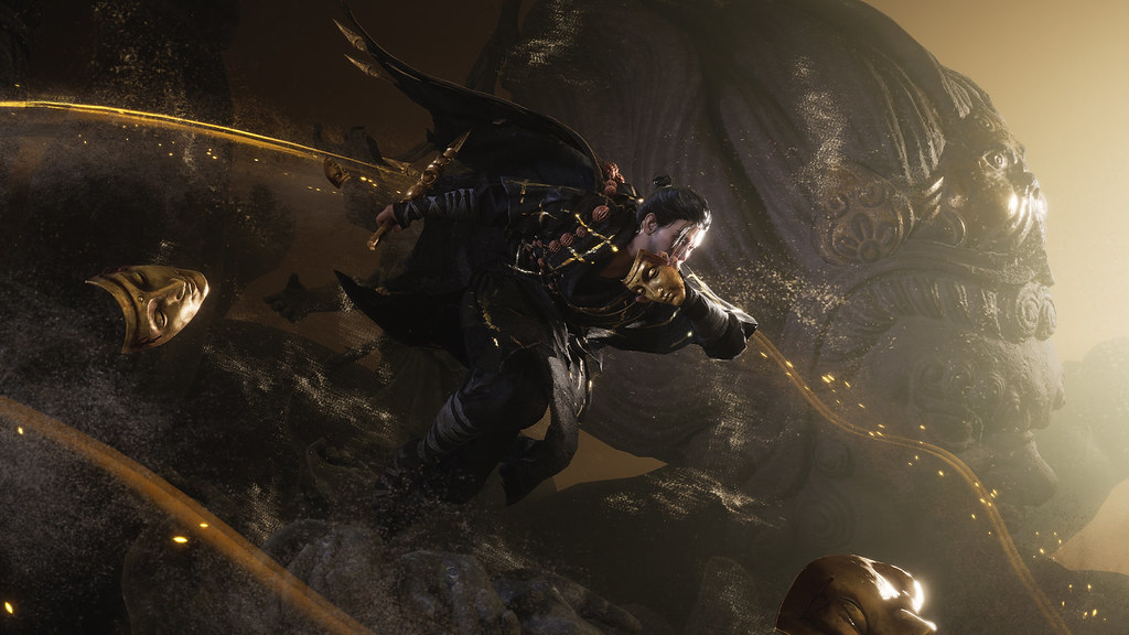 In this image, a black and gold clad figure leaps from left to right, clutching a gold mask by their face with their left hand, and a gold dagger-like weapon in their right.