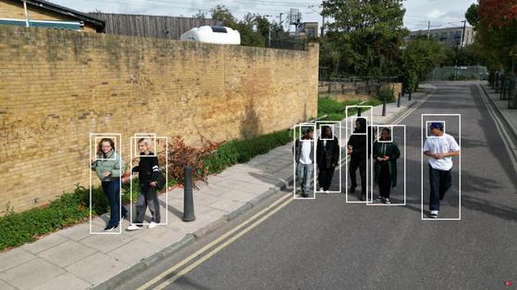 A group of people are passing each other in the street with a surveillance overlay of white box outlines.