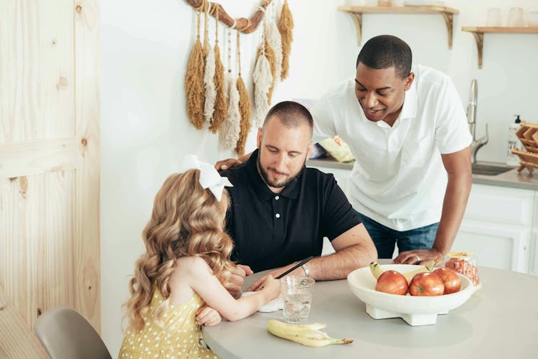 A pair of dads chat with their daughter at the table.