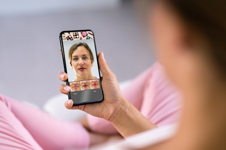 a woman holds a mobile phone showing her face with make up on