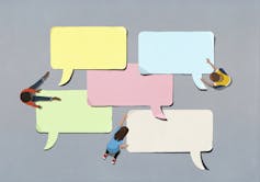 Seen from above, three kids arrange big paper speech bubbles on the ground.