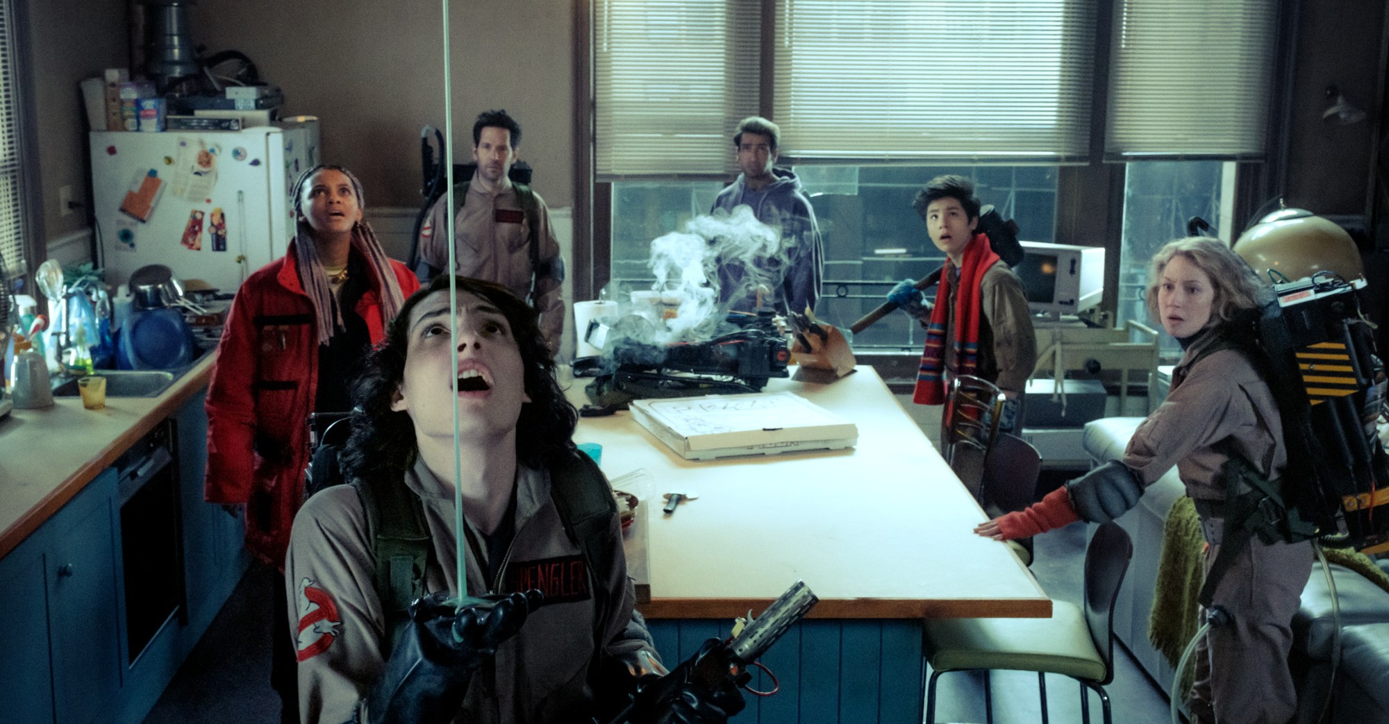 Finn Wolfhard in a Ghostbusters uniform looking at slime coming from the ceiling while Kamail Nanjiani, Logan Kim, Paul Rudd, and Celeste O’Connor stand behind him in Ghostbusters: Frozen Empire