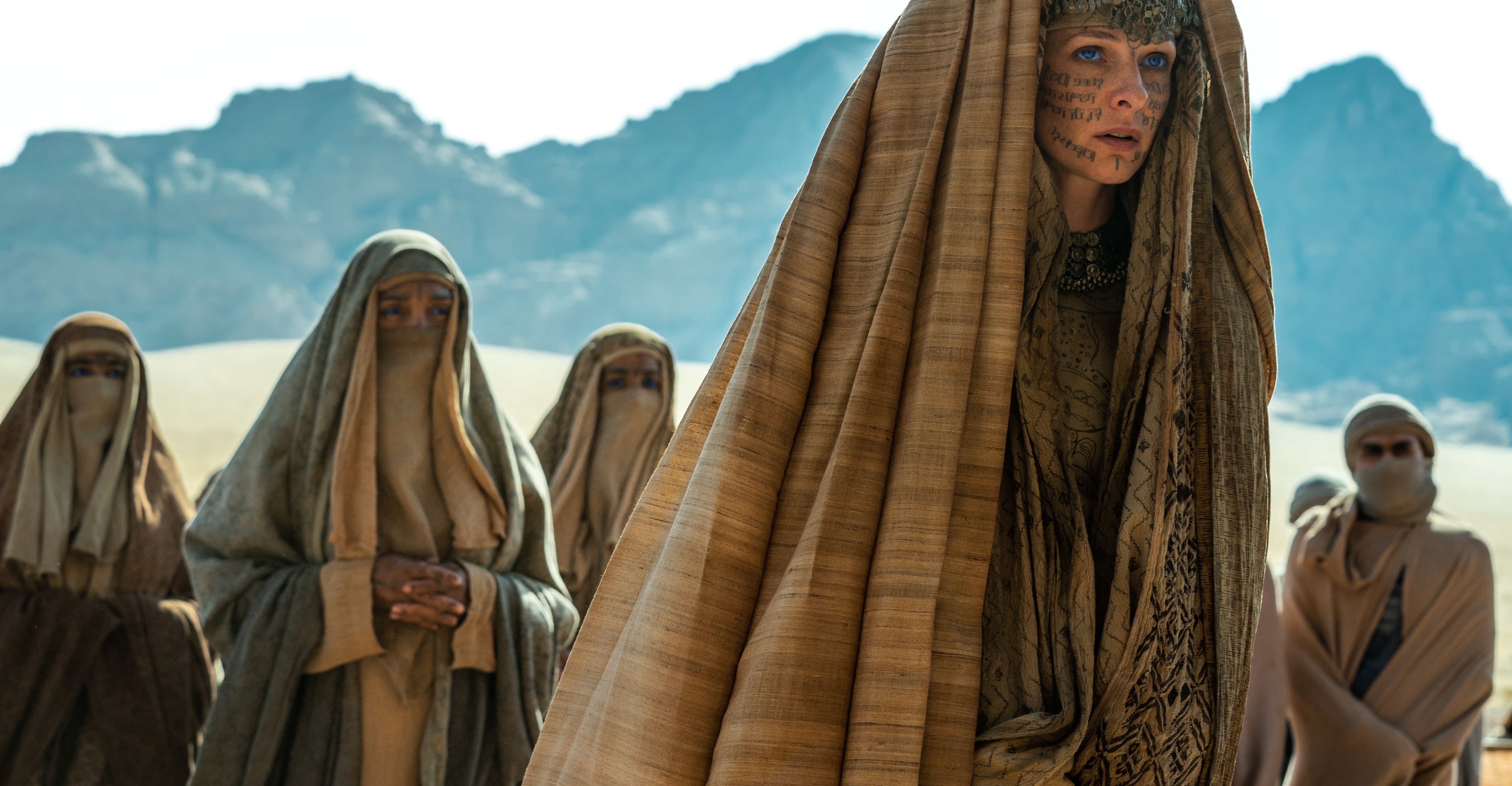 Lady Jessica (Rebecca Ferguson), cowled and with symbols written across her face in ink, stands in the desert, surrounded by similarly robed figures in Denis Villeneuve’s Dune: Part Two