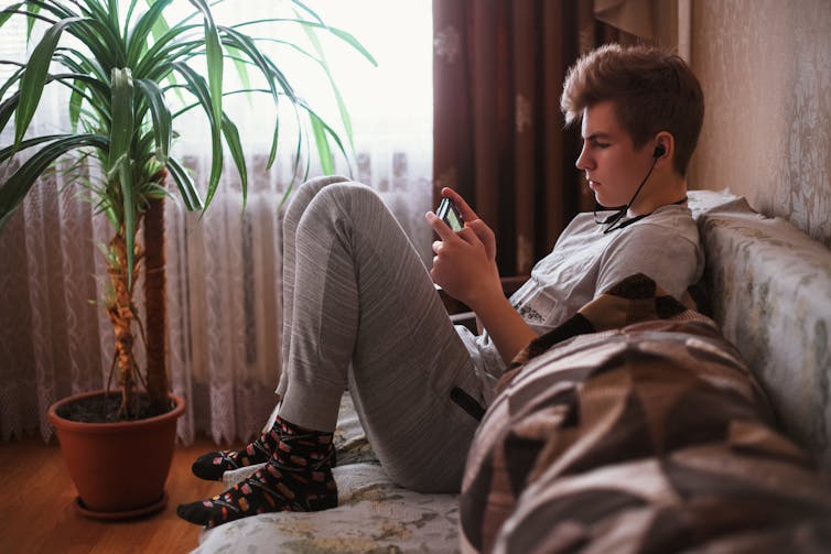 A teenager sits on a couch and watches their smartphone