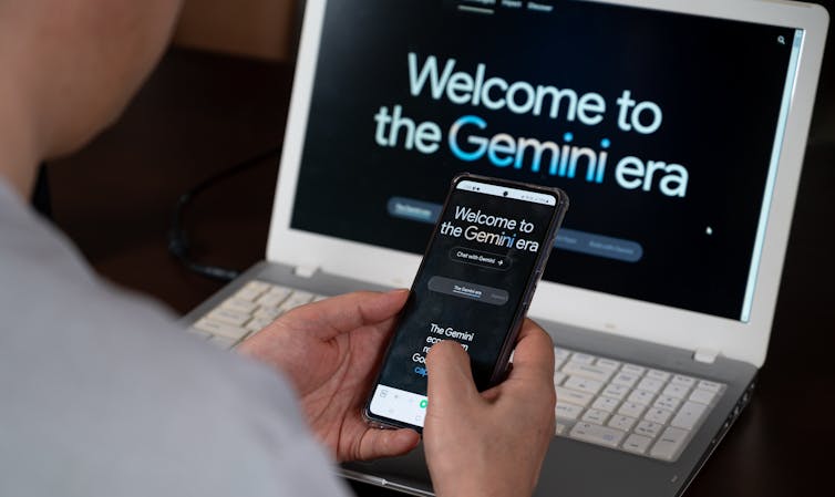 A person using Google Gemini on a smartphone while the Gemini landing page is seen on a laptop screen in the background