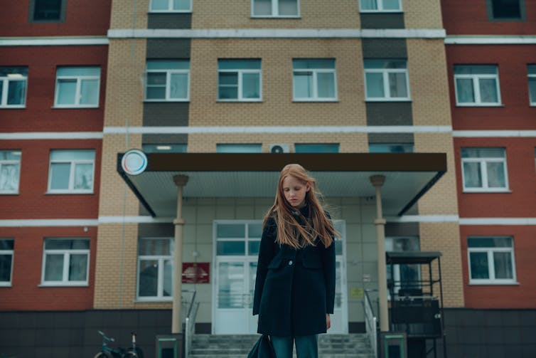 Girl looks sad outside large building