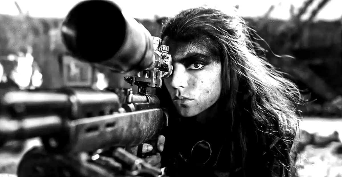 A young woman with black war paint on her forehead stares through the scope of a rifle in Furiosa: A Mad Max Saga.A young woman with black war paint on her forehead stares through the scope of a rifle in Furiosa: A Mad Max Saga.