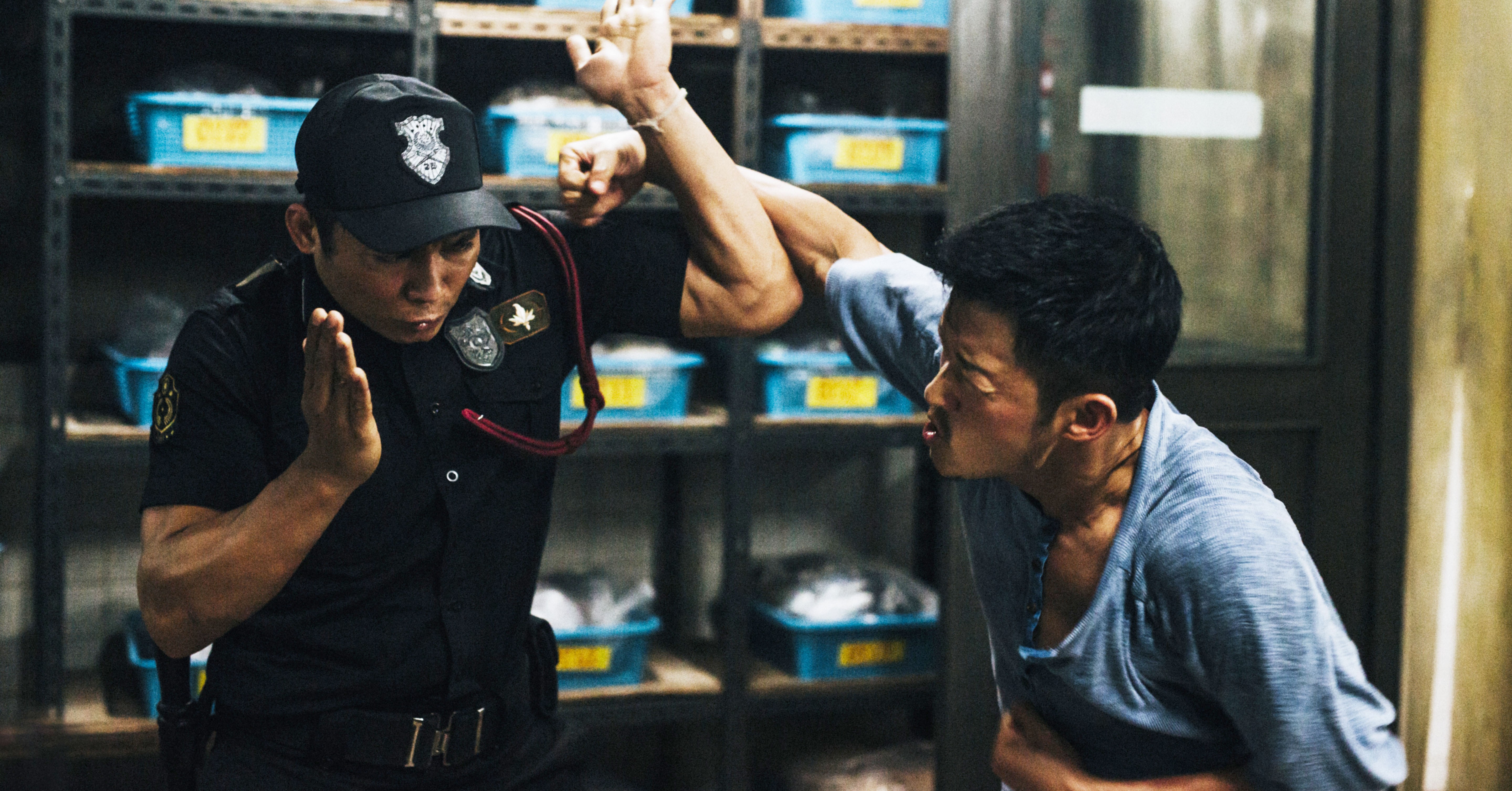 Two men stand in a garage fighting each other. One is wearing a police uniform and blocking a punch from the other who is wearing a blue shirt in SPL 2: A Time for Consequences, aka Kill Zone 2Two men stand in a garage fighting each other. One is wearing a police uniform and blocking a punch from the other who is wearing a blue shirt in SPL 2: A Time for Consequences, aka Kill Zone 2