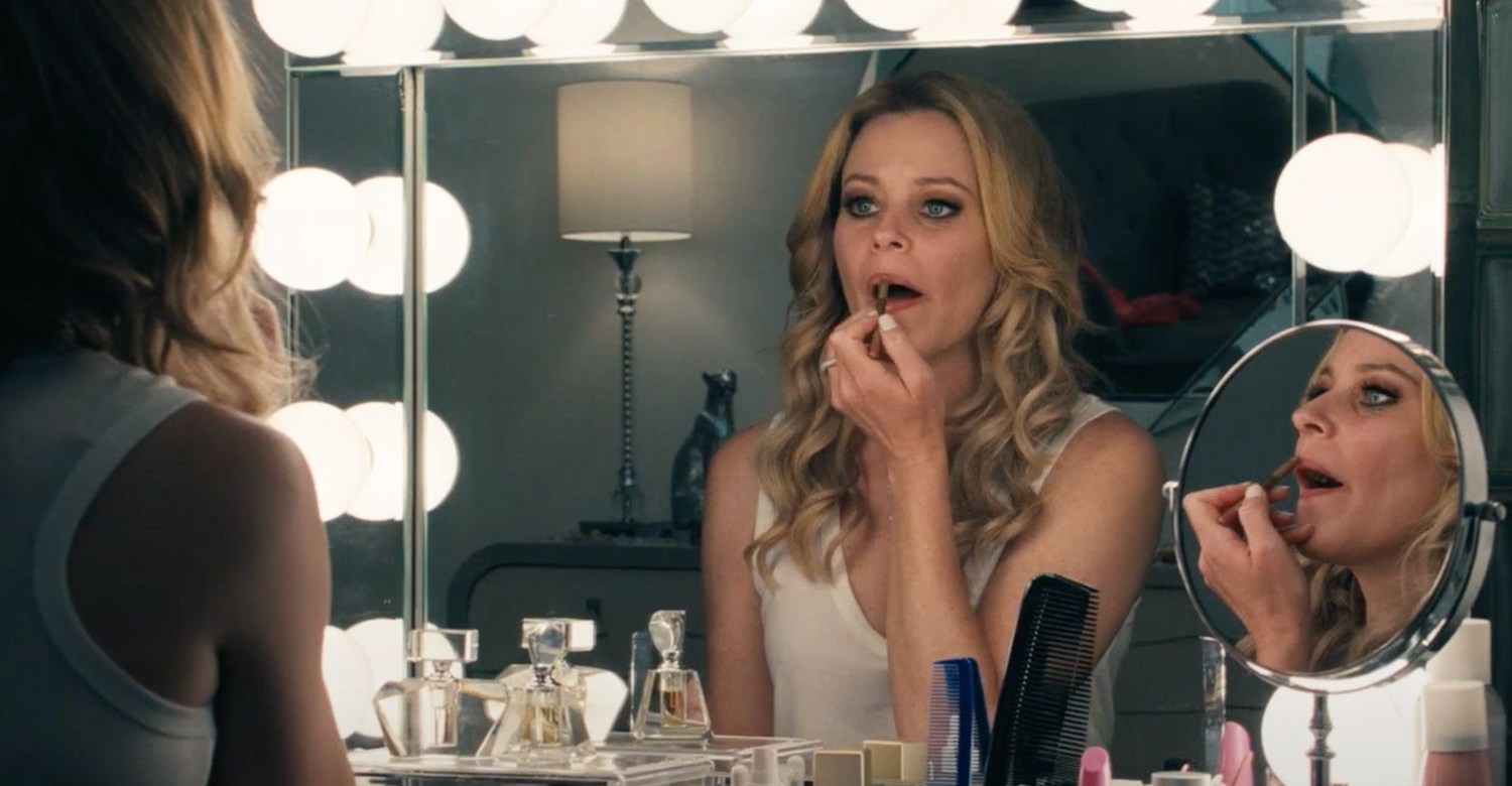 Elizabeth Banks applying lipstick in mirror in Skincare.