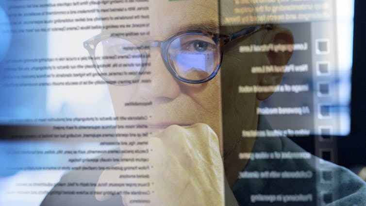 A man in glasses looks through a see-through screen with words in black font covering most of it.