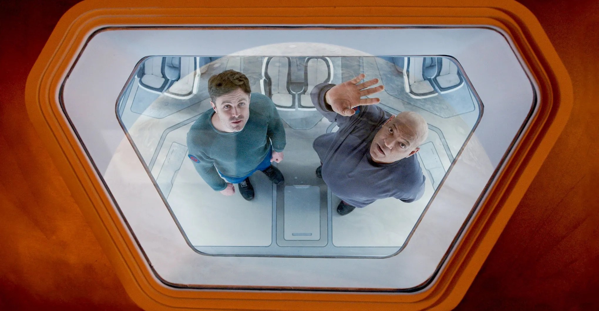 Casey Affleck and Laurence Fishburne staring up through the porthole of a spaceship at a nearby planet in Slingshot.